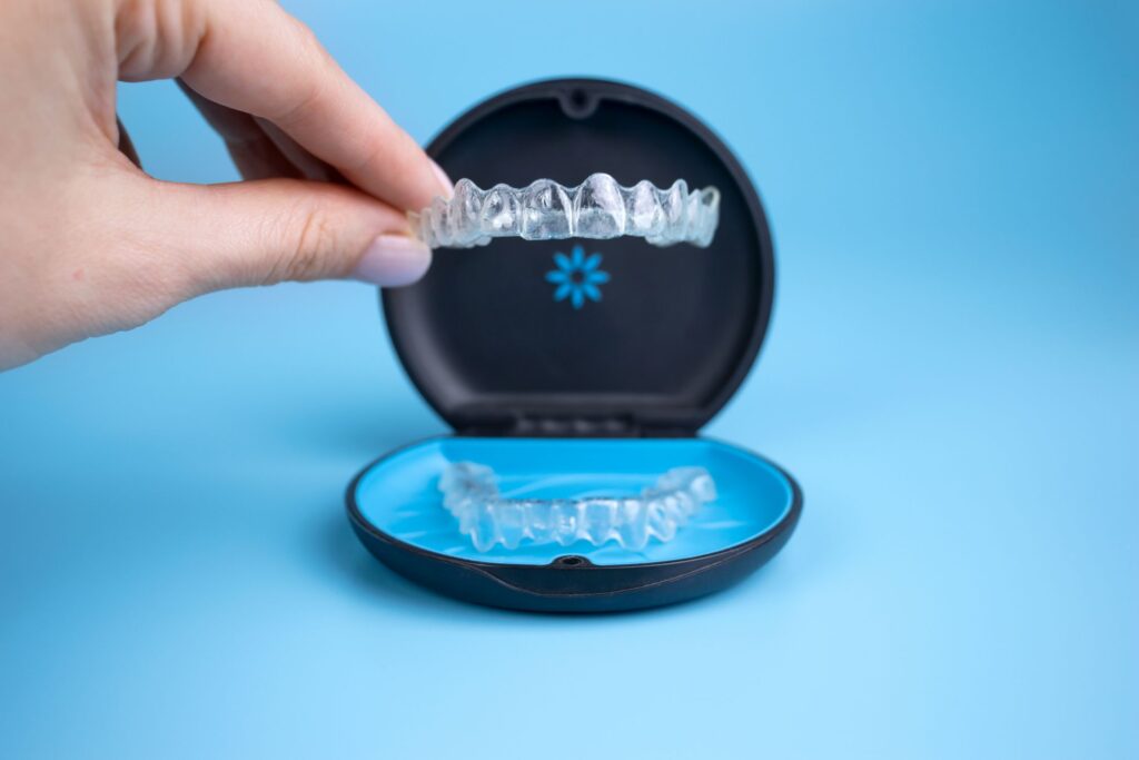 Fingers lifting Invisalign tray from its carrier case