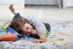 Child lying on rug sucking thumb among toys.